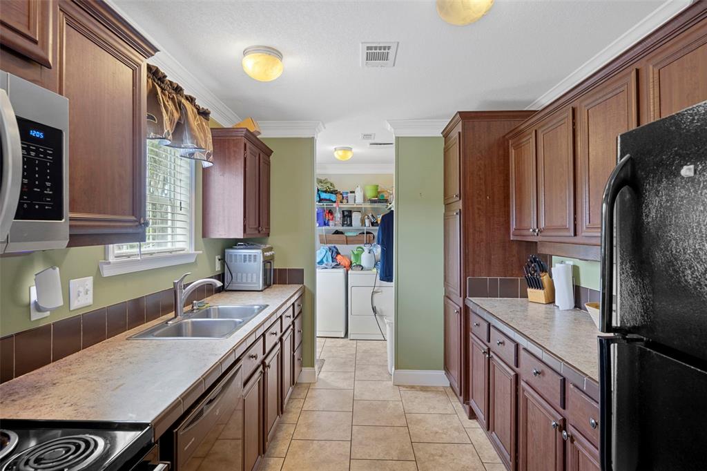 Galley kitchen offers abundant cabinet and counter space, darker wood-finish cabinetry, stainless steel appliances and tile flooring.