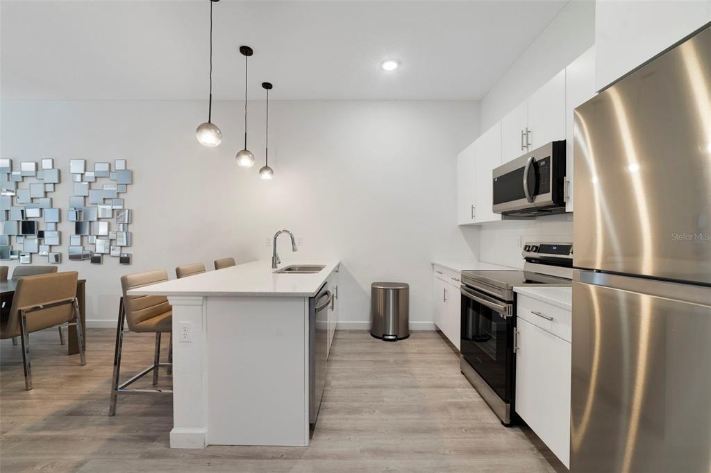 The open kitchen features STAINLESS STEEL APPLIANCES, sleek countertops, complementary cabinetry, tiled backsplash and a breakfast bar with pendant lighting perfect for casual dining or entertaining.