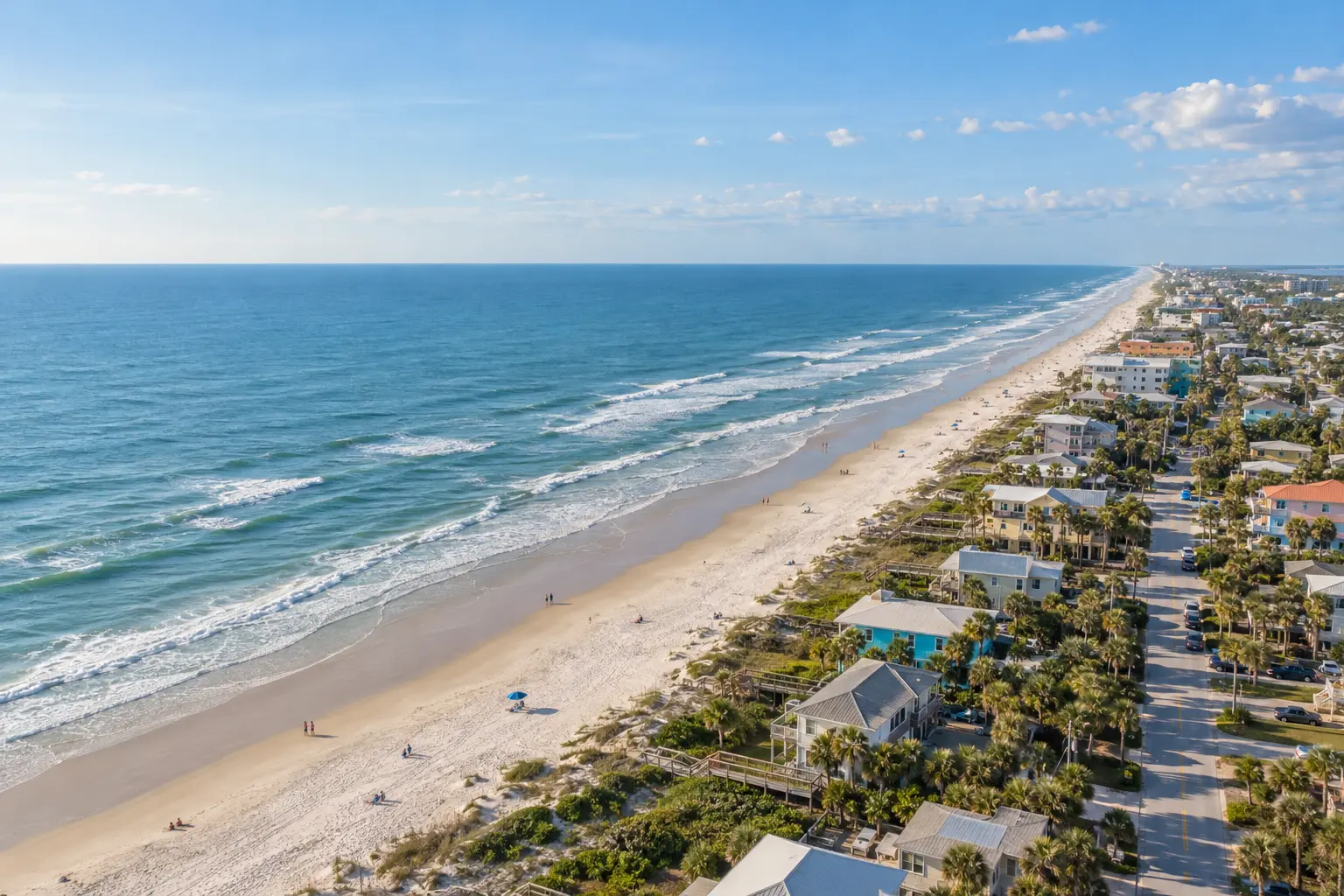 Elevated coastal view of New Smyrna Beach, with Atlantic surf, a broad sandy shoreline and low-rise beachside streets near Flagler Avenue.